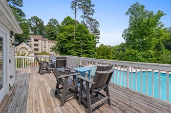 A wooden deck with chairs and a table overlooking a pool.